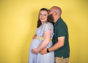 Couple embraces sweetly against bright yellow backdrop in romantic engagement photo shoot series.