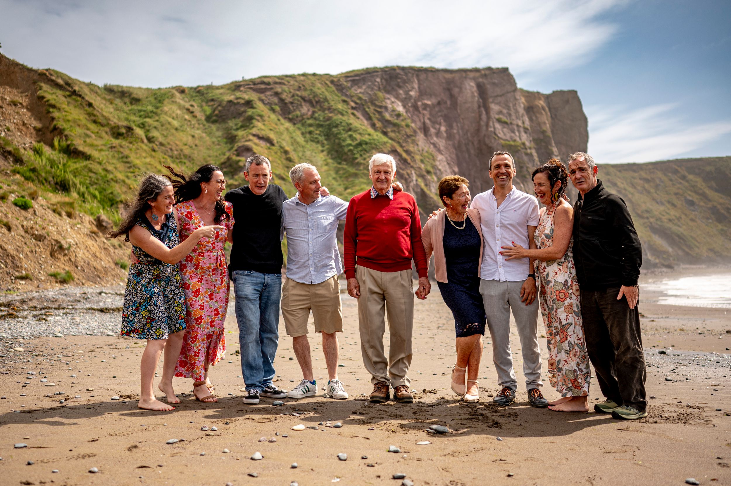 extended family of 9 adults smiling together on a ballydwan beach waterford with dramatic green cliffs in the background on a sunny day