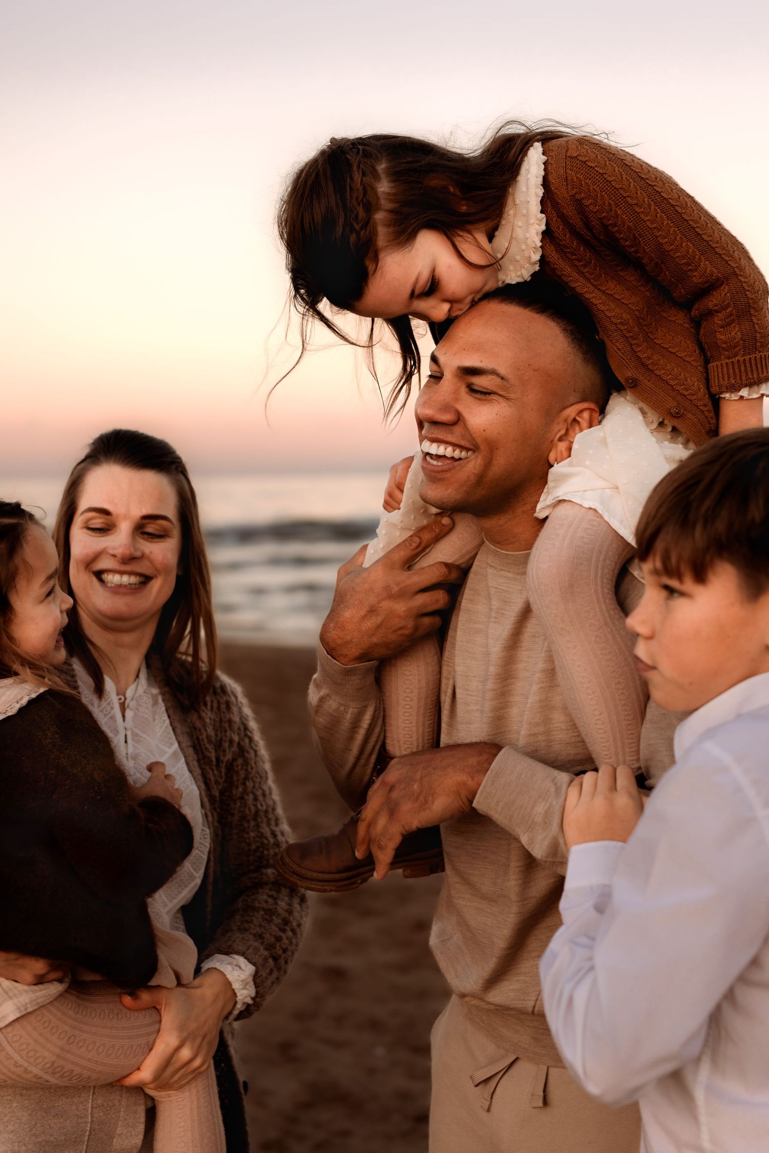 A happy family wearing neutral tones shares joyful moments together on the beach at sunset in Javea. Javea family photographer