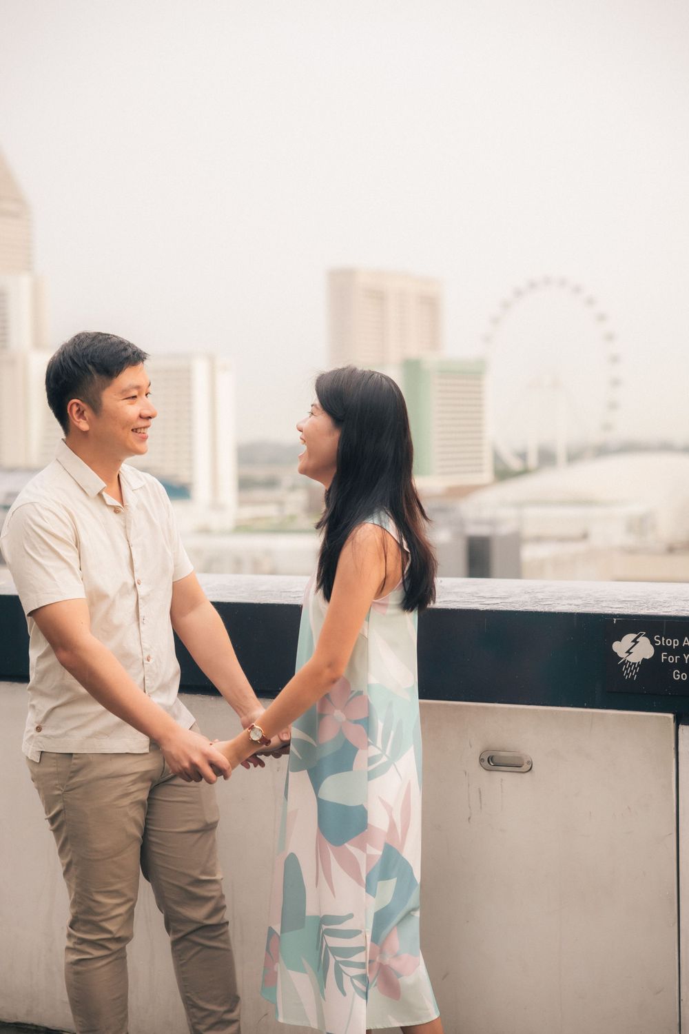 A couple shares a joyful moment on a rooftop with Singapore's skyline and the iconic Ferris wheel visible in the background.