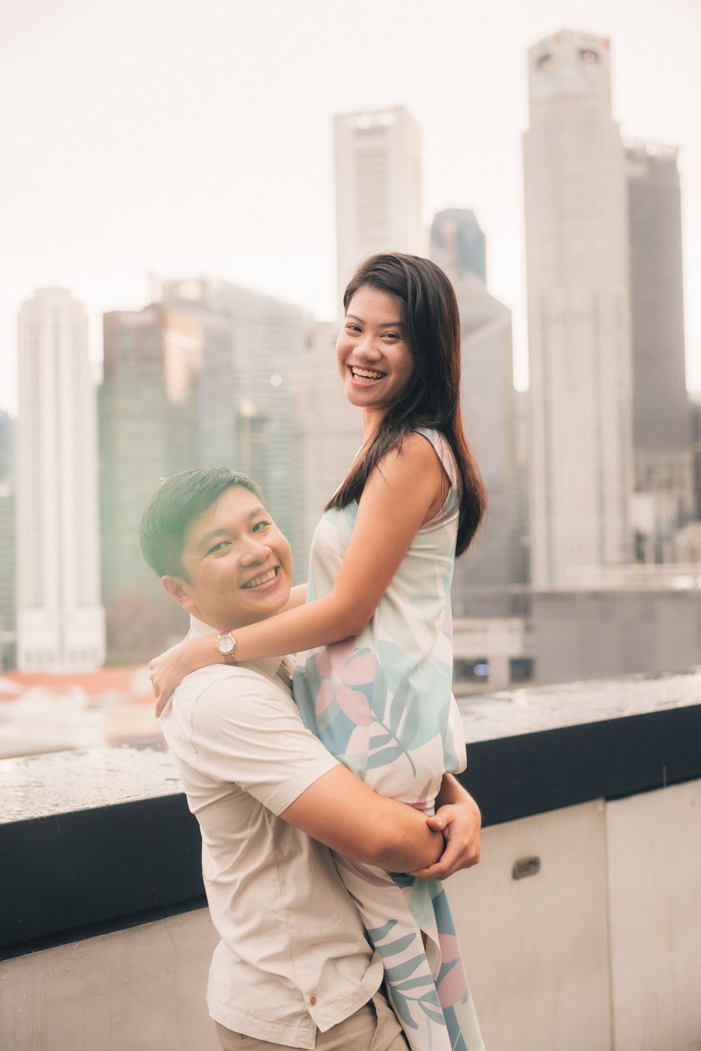 A couple shares a joyful embrace on a rooftop with city skyscrapers visible in the background.