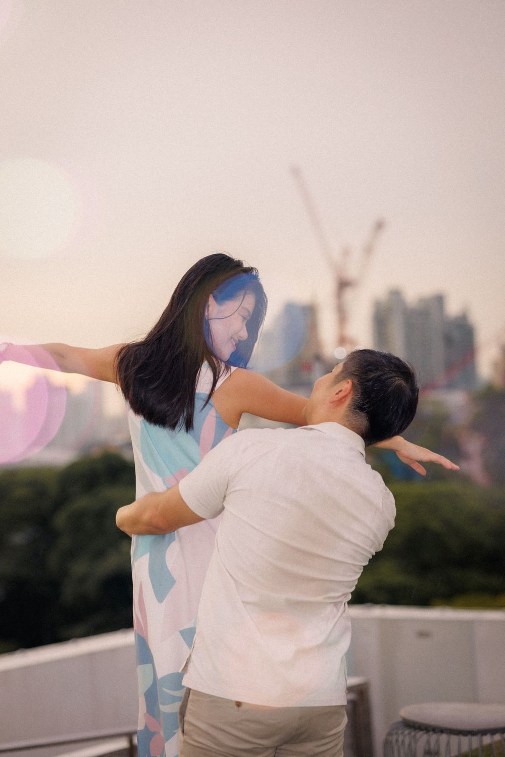 A playful couple embraces in a lifting pose against an urban skyline backdrop during golden hour.