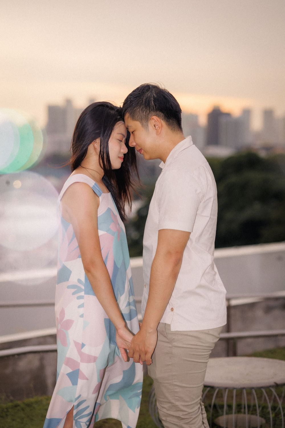 A romantic couple shares an intimate moment at sunset with a city skyline in the background.