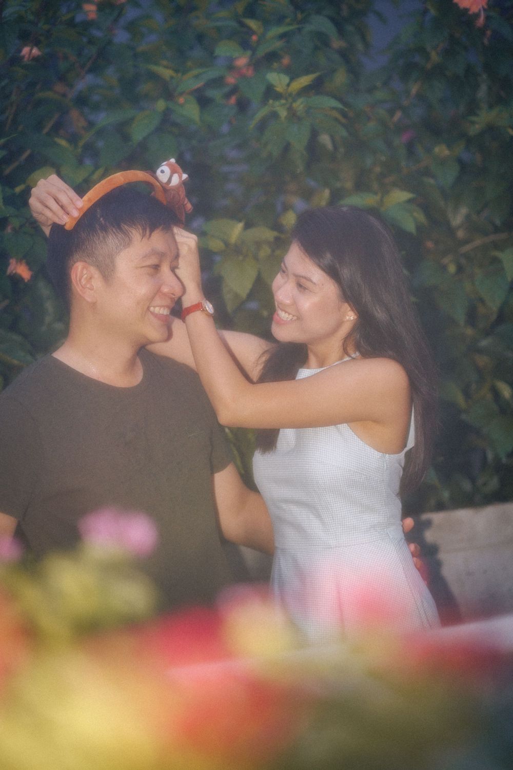 Romantic couple shares an intimate moment in a garden setting with soft bokeh and floral elements in the foreground.