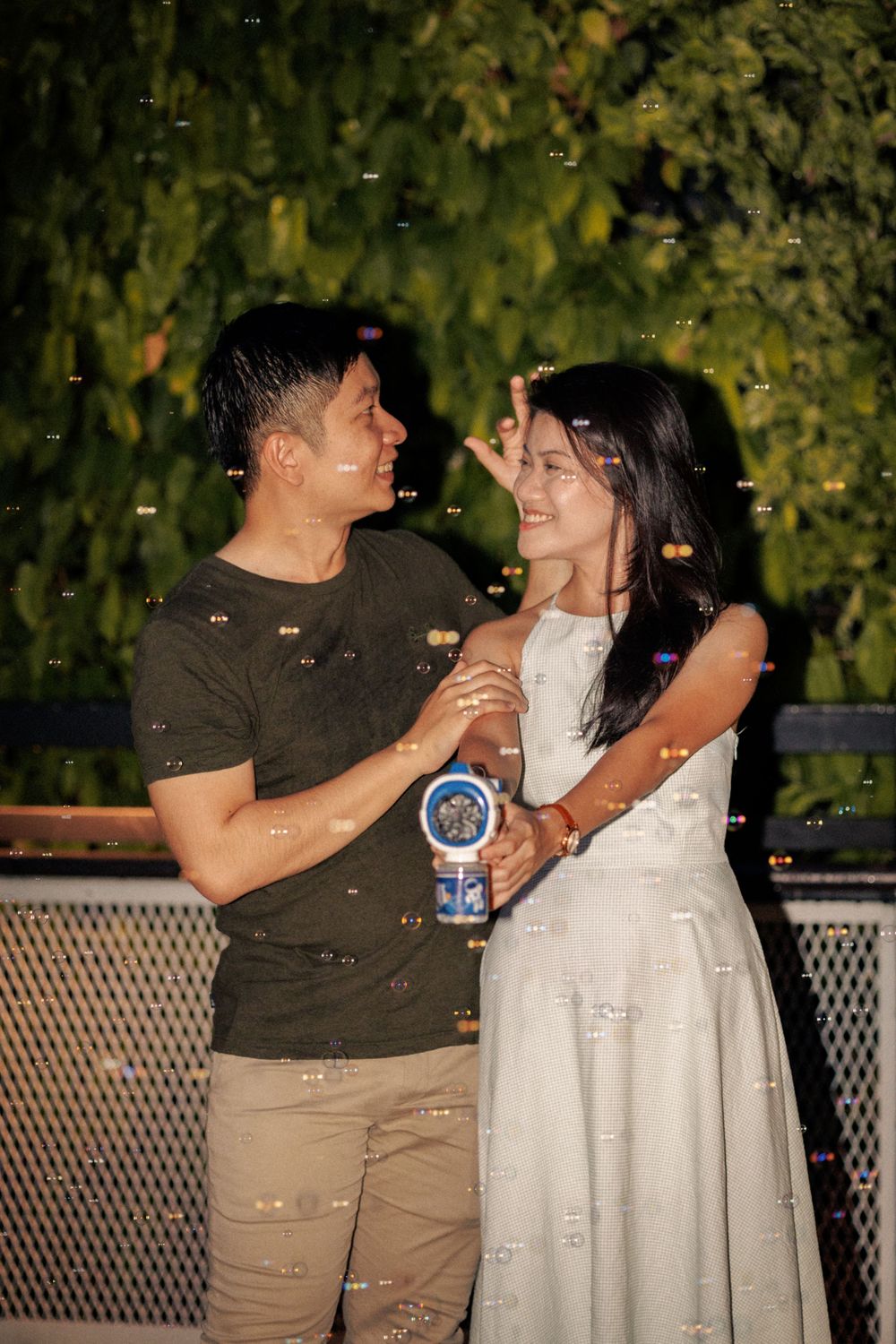 A couple laughs together during a nighttime photoshoot with bubble effects in the background.