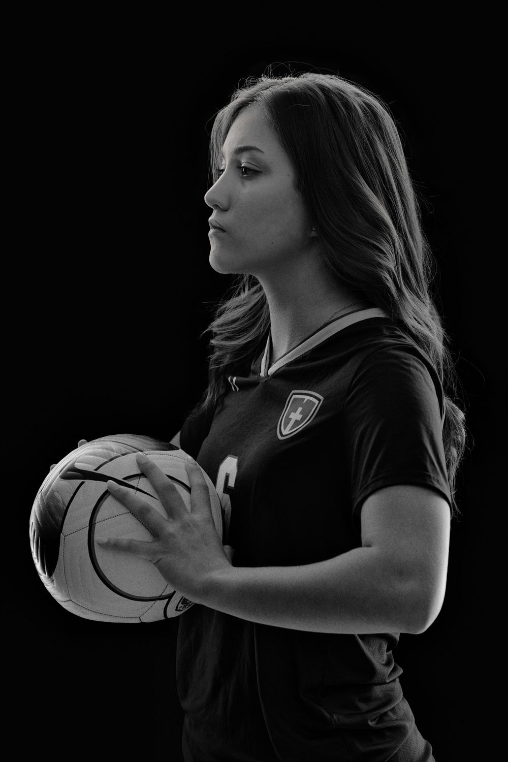 Young female with a soccer ball posing on a black backdrop photo in black and white.