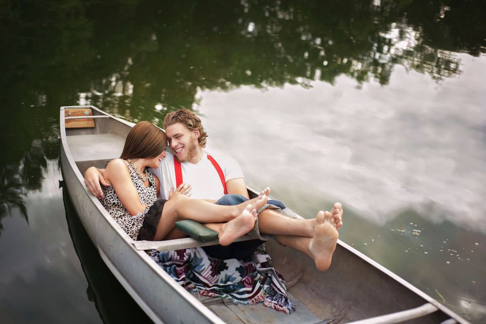A Notebook-inspired photoshoot, a couple in a boat embracing, the man is wearing suspenders, the female in animal print.