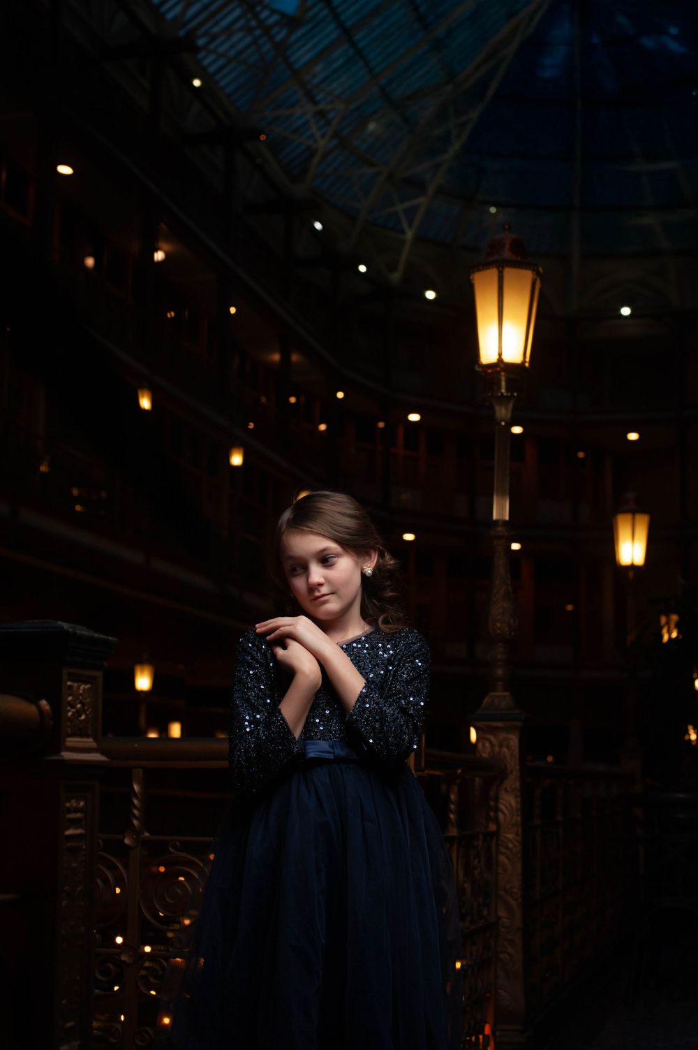 A young girl in a dark blue, floor-length dress is photographed at The Arcade located on Euclid Ave, Cleveland, OH 44111. Twinkle Lights