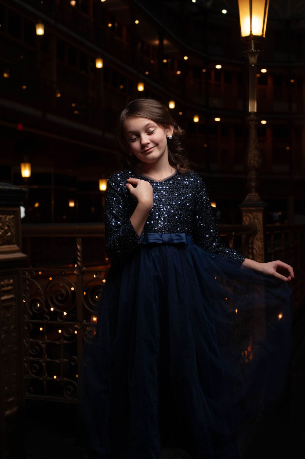 A young girl in a dark blue, floor-length dress is photographed at The Arcade located on Euclid Ave, Cleveland, OH 44111. Twinkle Lights