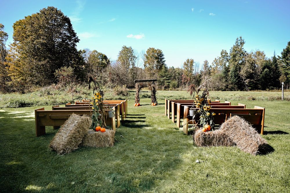 Rustic outdoor wedding venue with wooden pillars and stone decorations arranged in rows on a grassy field.