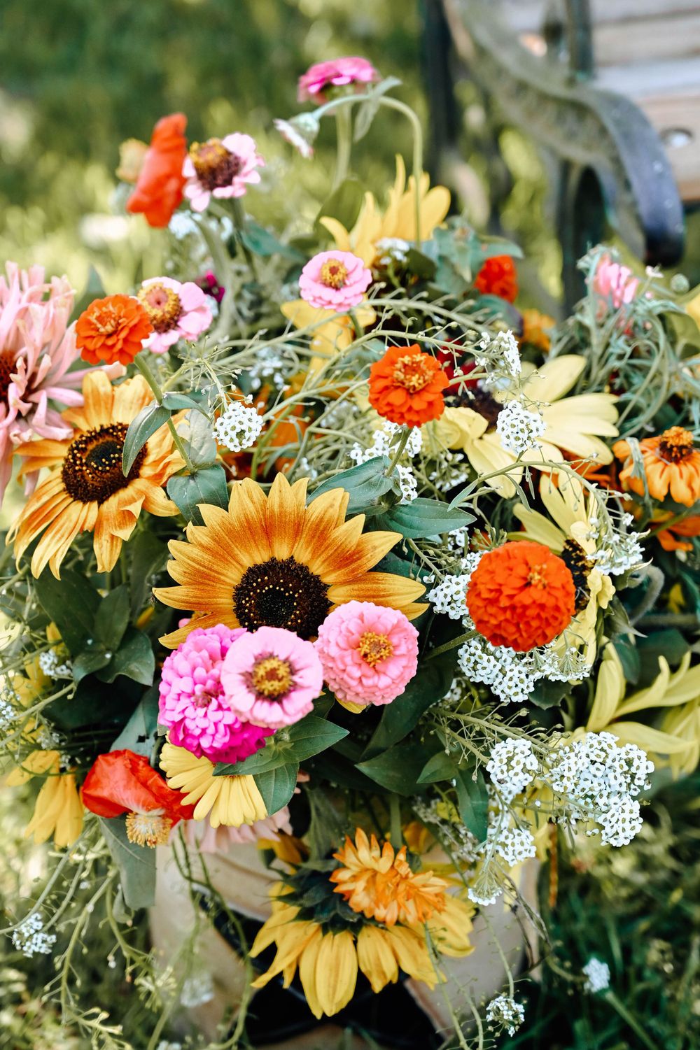 Vibrant bouquet of yellow sunflowers, orange zinnias, pink zinnias and delicate white Queen Anne's lace flowers in garden setting.