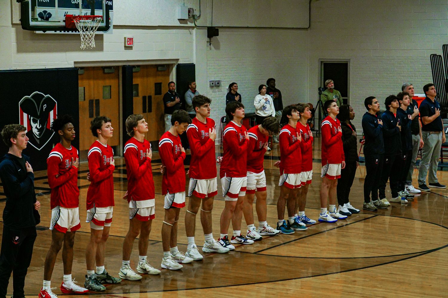 Basketball team in red uniforms stands in line during pre-game ceremony in gym.