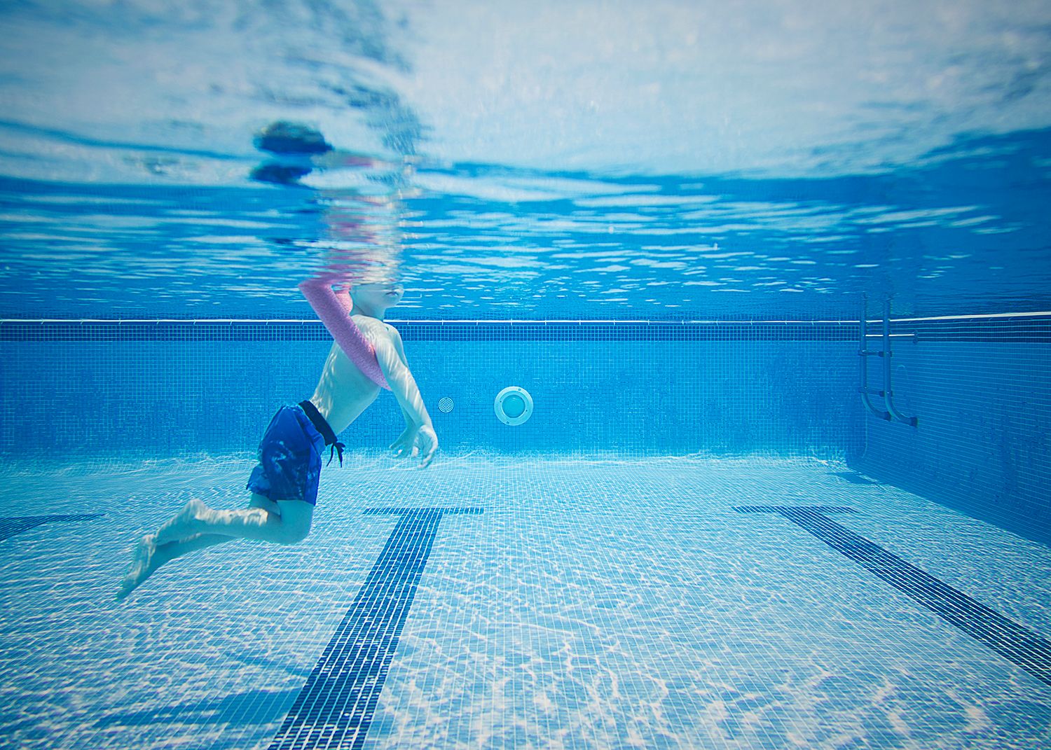 Underwater view of a swimmer gliding through a crystal clear swimming pool with blue rippling water.
