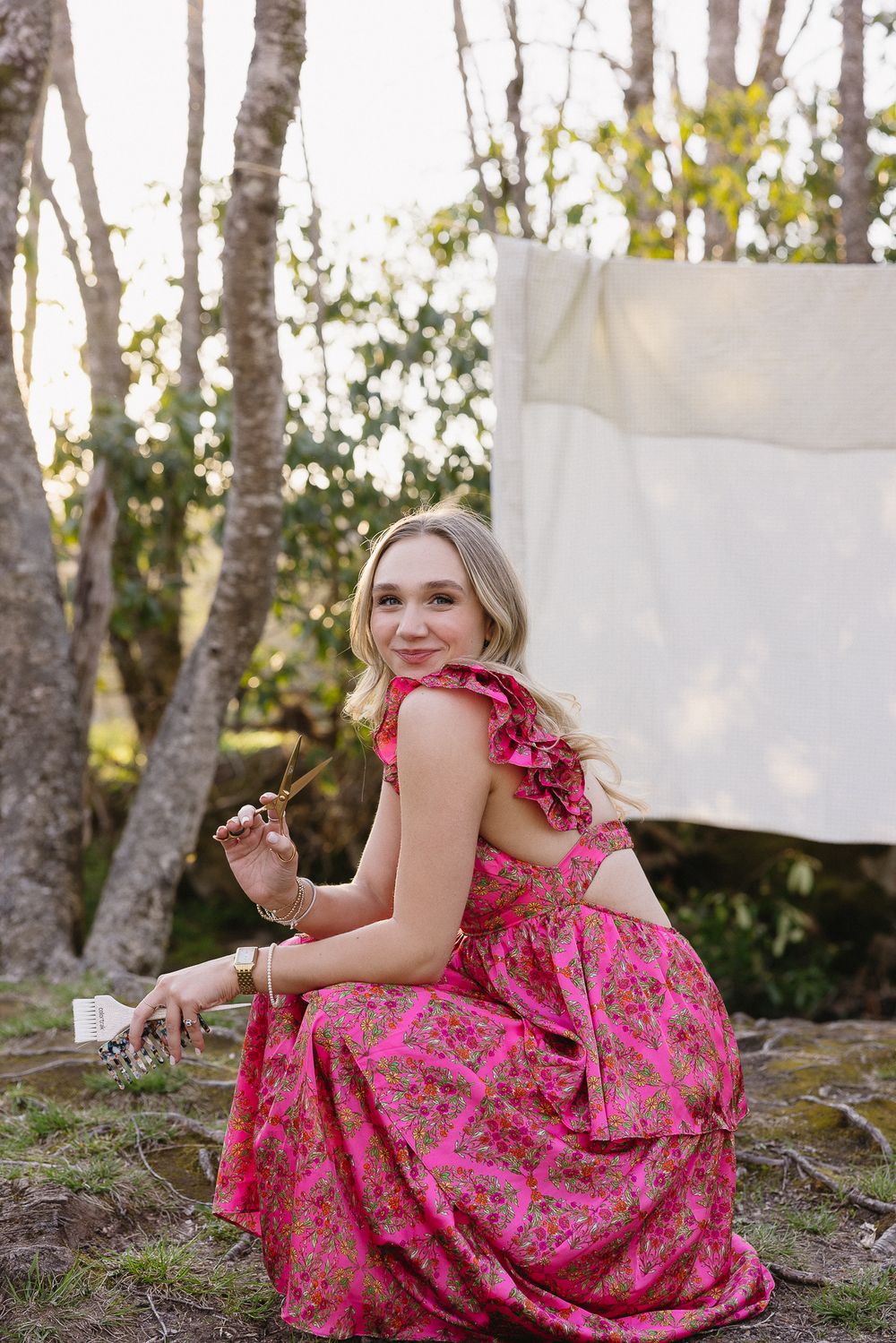 A person in a bright pink floral dress poses against a backdrop of birch trees and white sheets. The Bradford Wedding Photographer