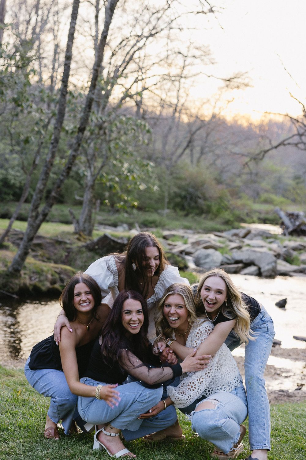 Friends laughing together by a stream during golden hour. The Bradford Wedding Photographer