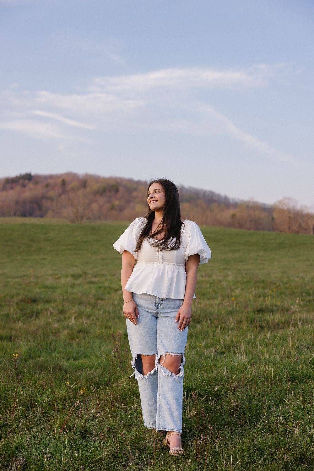 Woman in white blouse and ripped jeans standing in sunny meadow. Separk Mansion Wedding Photographer