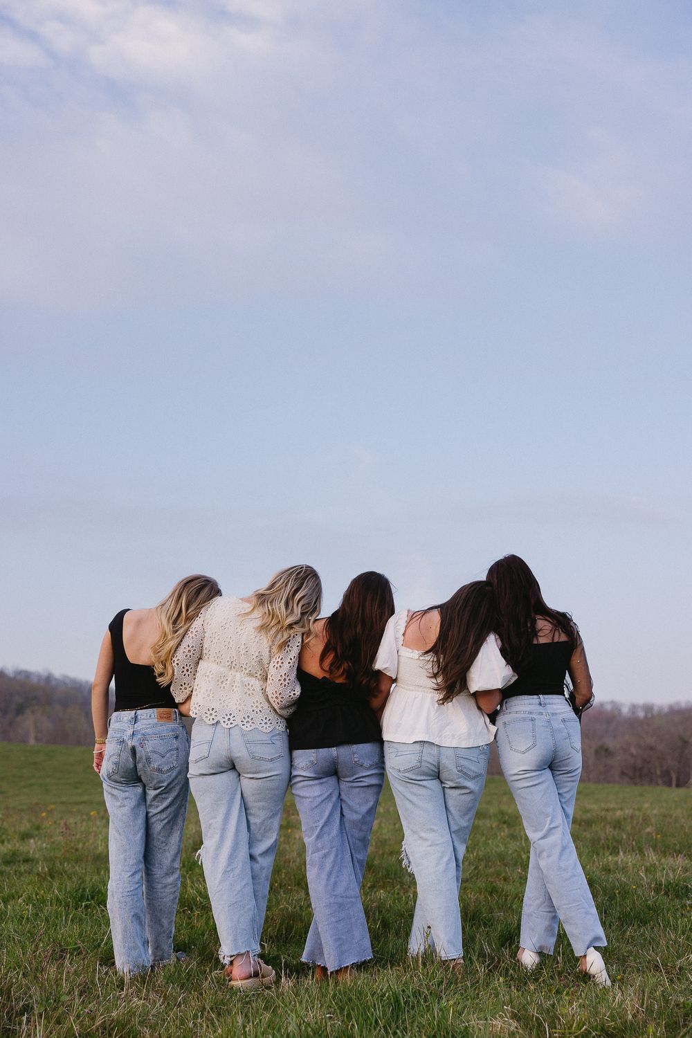Friends in denim jeans lined up showing their backs to camera in a grassy field. The Bradford Wedding Photographer