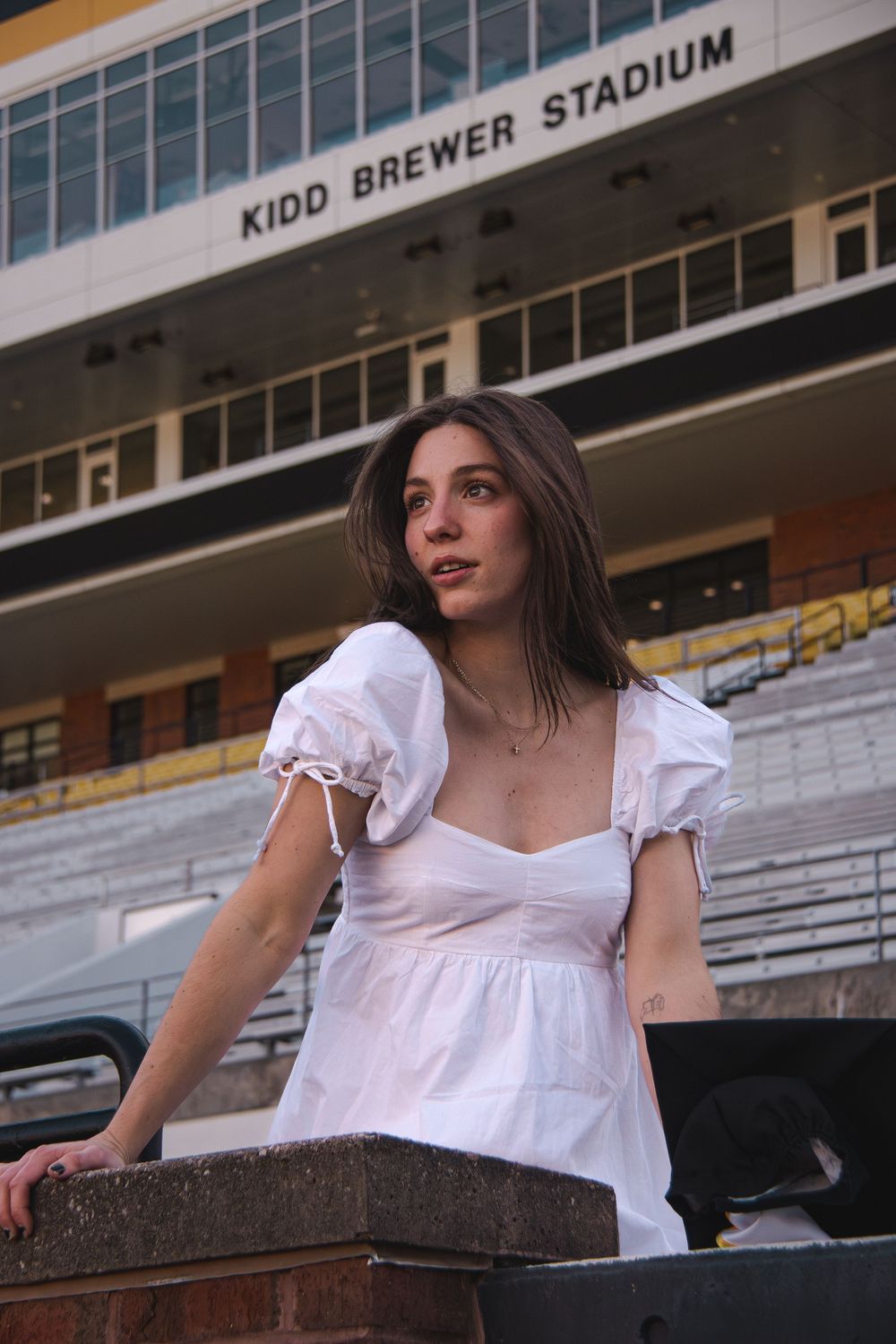 Person in white dress posing on bleachers at Kidd Brewer Stadium. Luxury wedding photographer North Carolina