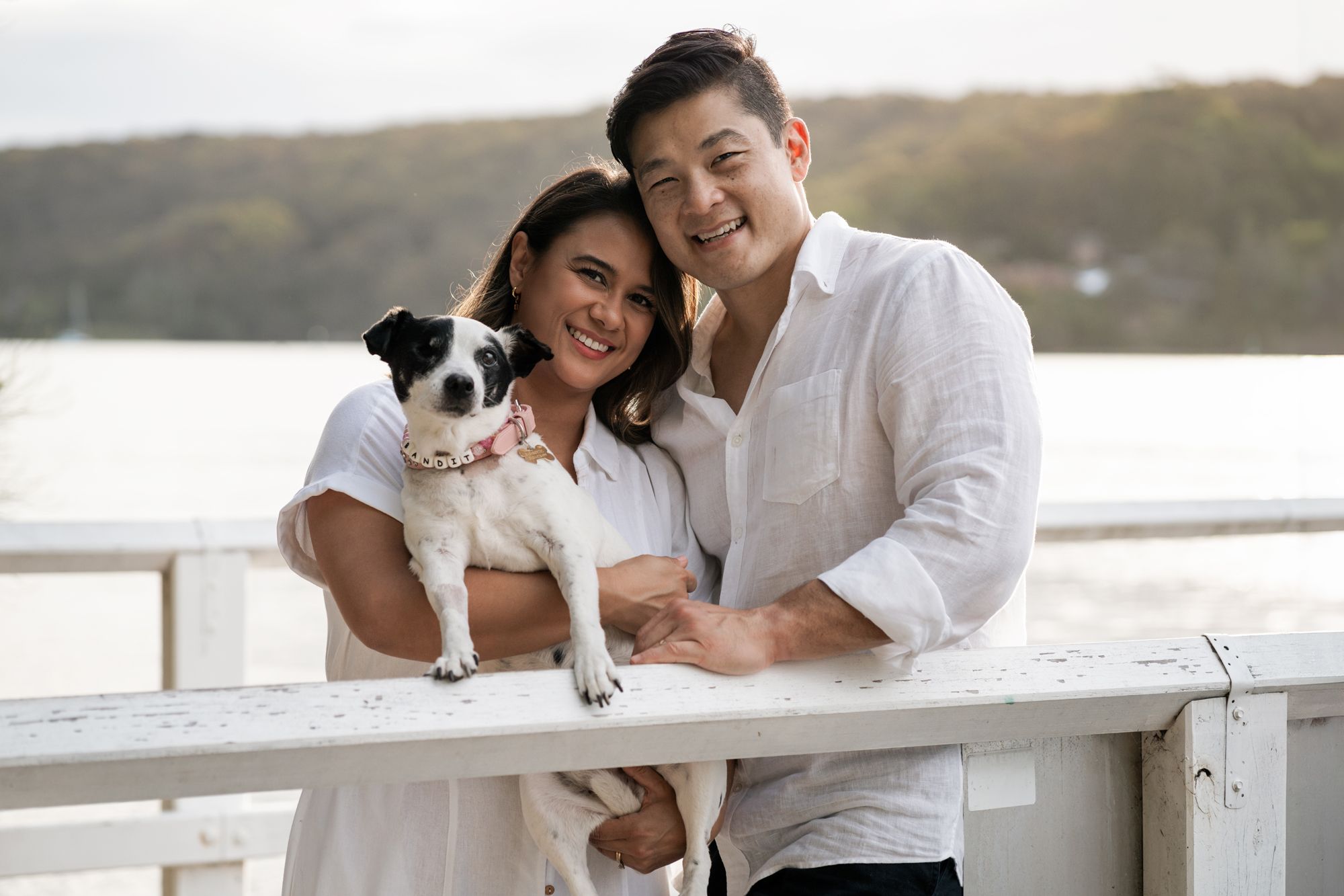 Couple smiling and looking directly to the camera while holding their sweet little dog in Sydney family photoshoot