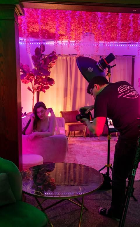 Photography crew setting up equipment in a room with pink lighting and white curtains.