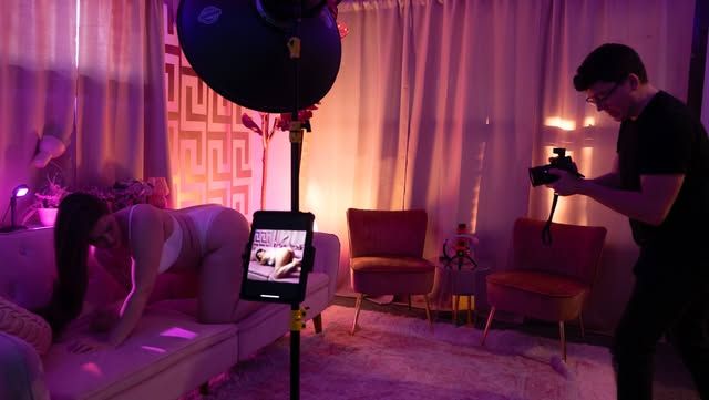 Behind-the-scenes view of studio photography equipment and monitors in purple lighting.