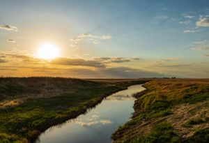 Golden sunset over meandering river with dramatic clouds and grassy embankments.