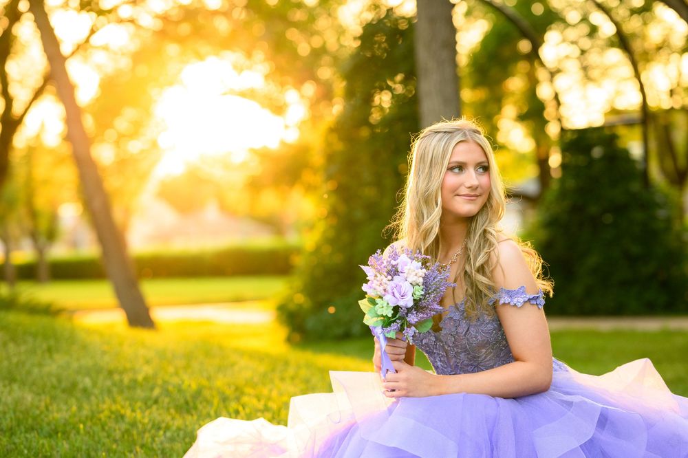 A person in a floral dress stands in a sunlit garden with golden light filtering through the trees at sunset.