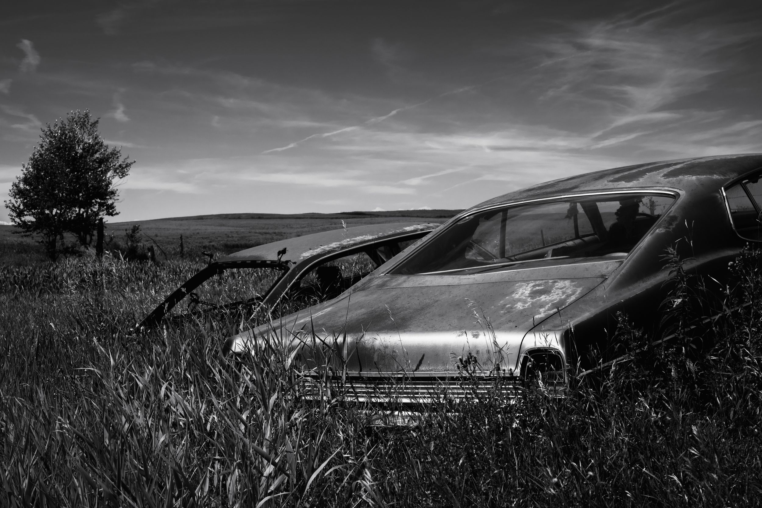 Dramatic black and white landscape with silhouetted car against rolling hills and moody sky at sunset.