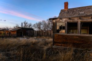 Abandoned wooden house with rustic charm at dusk against a pink-tinged sky.