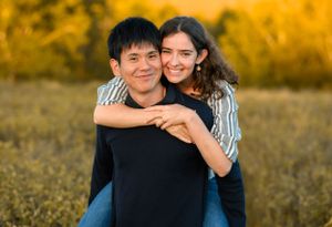 A couple poses playfully in a golden sunlit field during sunset.