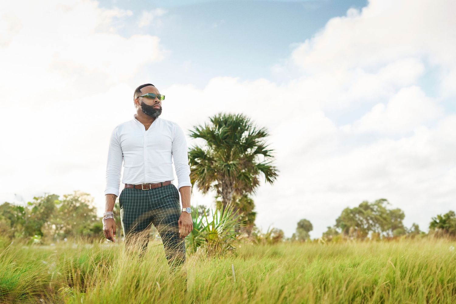 A scenic outdoor portrait in a grassy field with palm trees and blue sky.