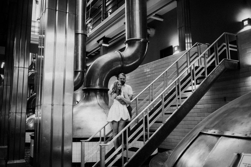A black and white industrial photograph showing large metal pipes and stairways in a manufacturing facility.