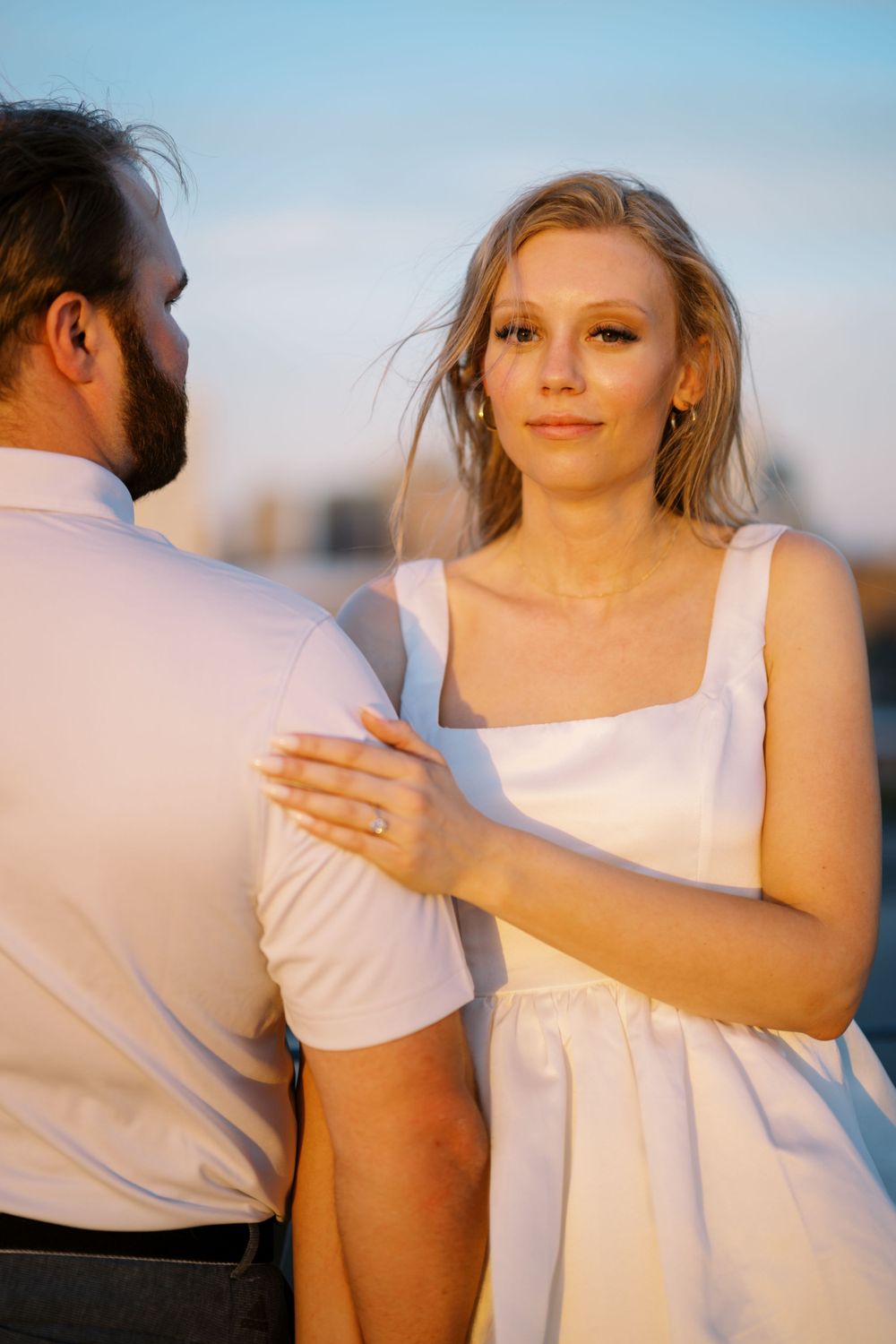 A couple in white clothing embrace during golden hour with soft lighting and a dreamy atmosphere.