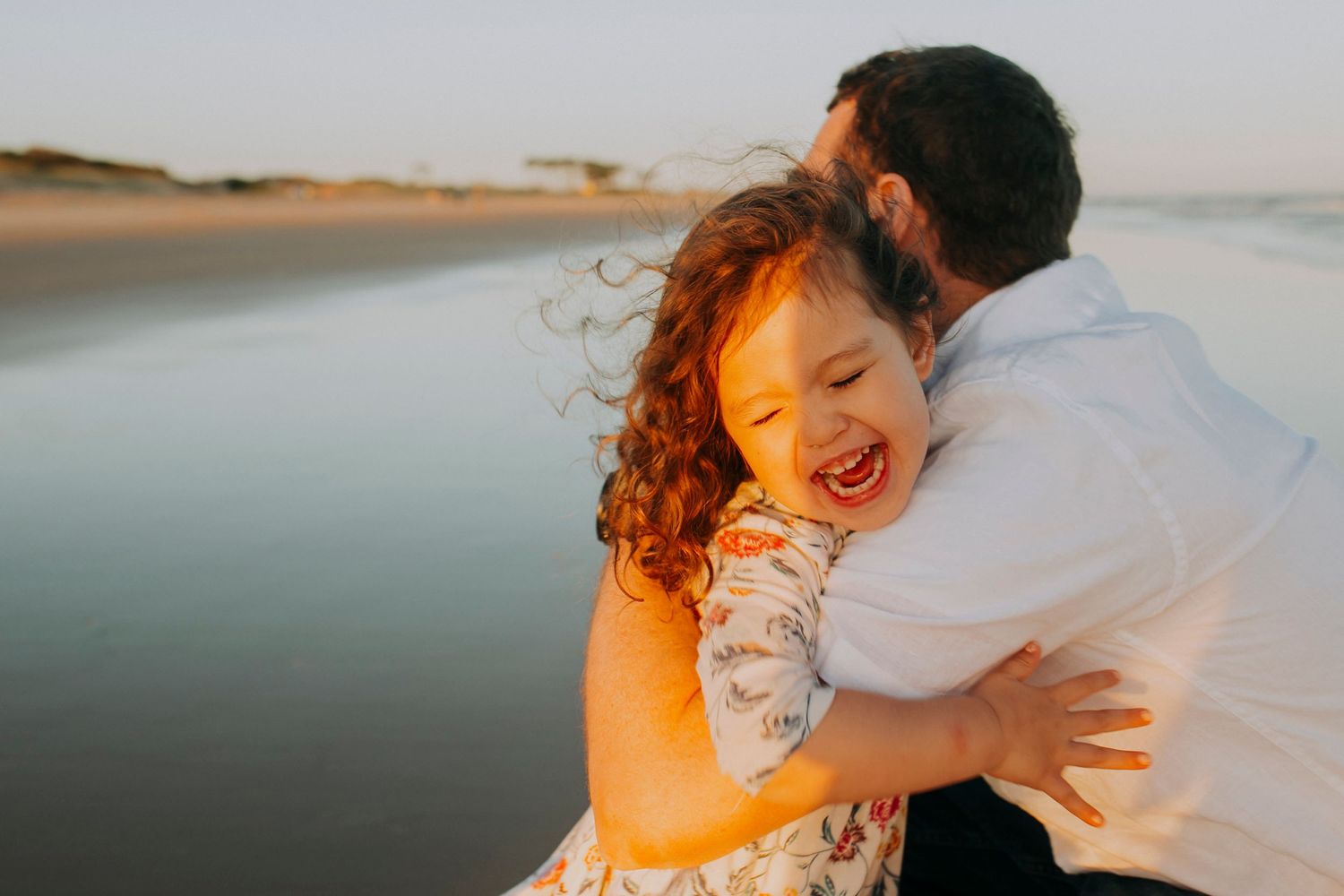 A cheerful moment captured during golden hour on a peaceful beach as sunlight illuminates joyful expressions and curly hair.