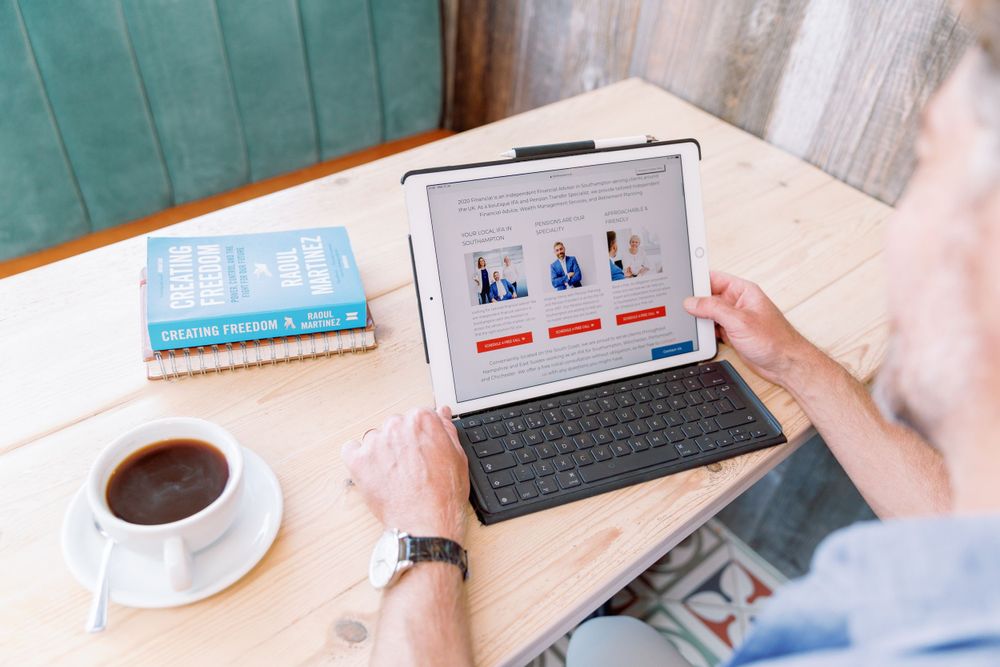 Person viewing business charts on tablet with keyboard while having coffee at wooden table.