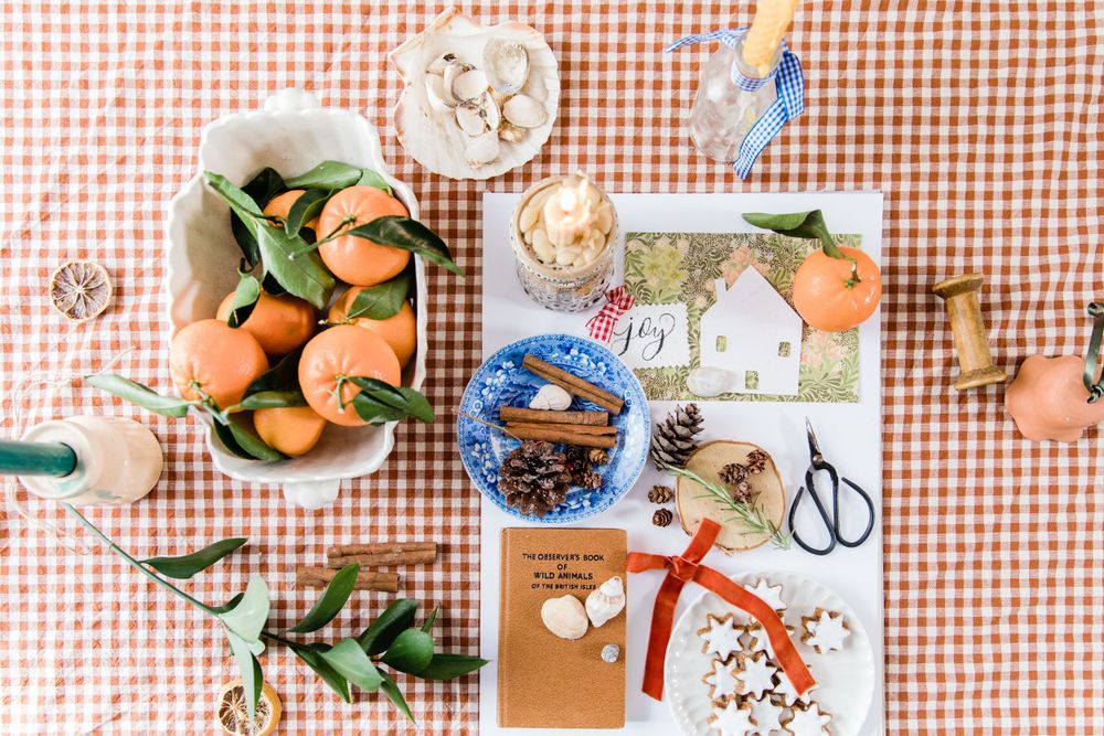 Flatlay of autumn crafting items and fresh oranges on a red gingham tablecloth.