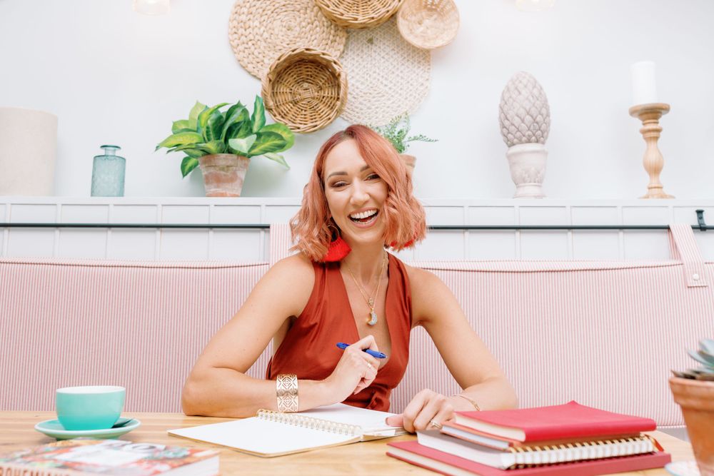 Woman with pink hair works at a desk with colorful stationery and home decor.
