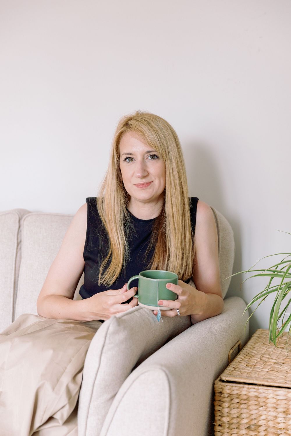 A person relaxes in a cozy armchair with a green mug, surrounded by houseplants and neutral decor.
