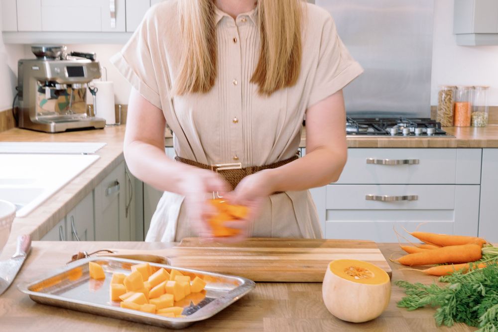A person slicing fresh carrots on a wooden cutting board in a bright white kitchen.