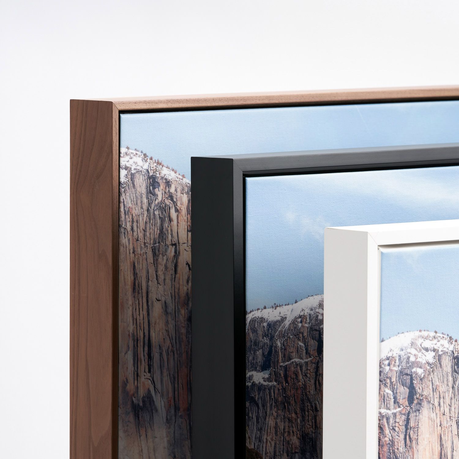 Close-up detail of three picture frames in wooden, black, and white finishes showing mountain landscape photos.