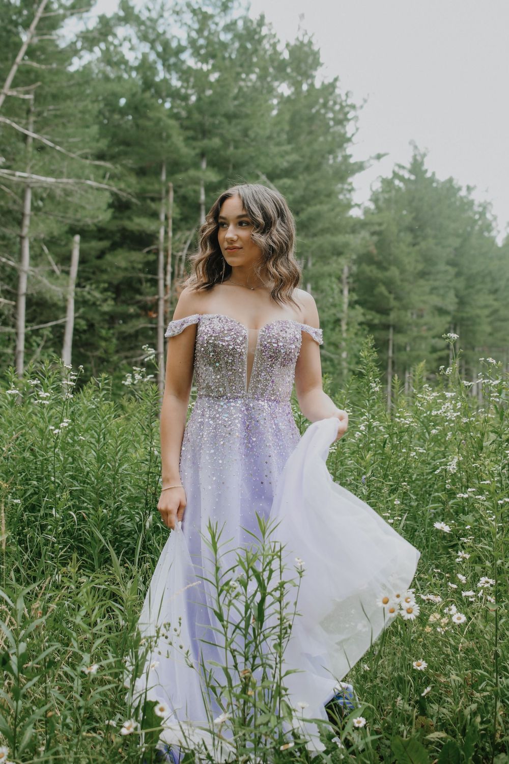 A sparkly lavender gown flows in a natural outdoor setting with pine trees.