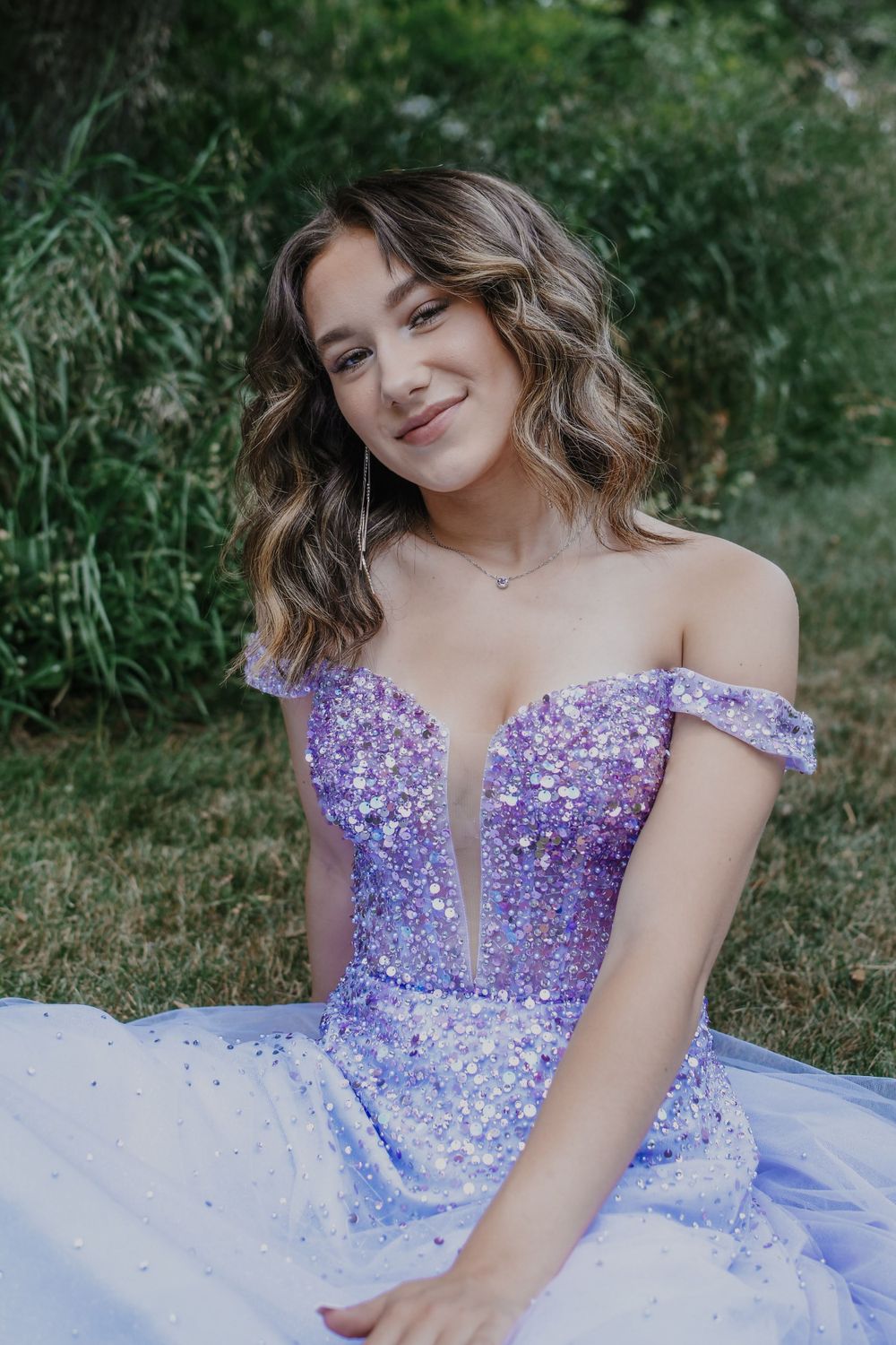 A lavender sequined off-shoulder ball gown with sweetheart neckline sparkles in an outdoor garden setting.