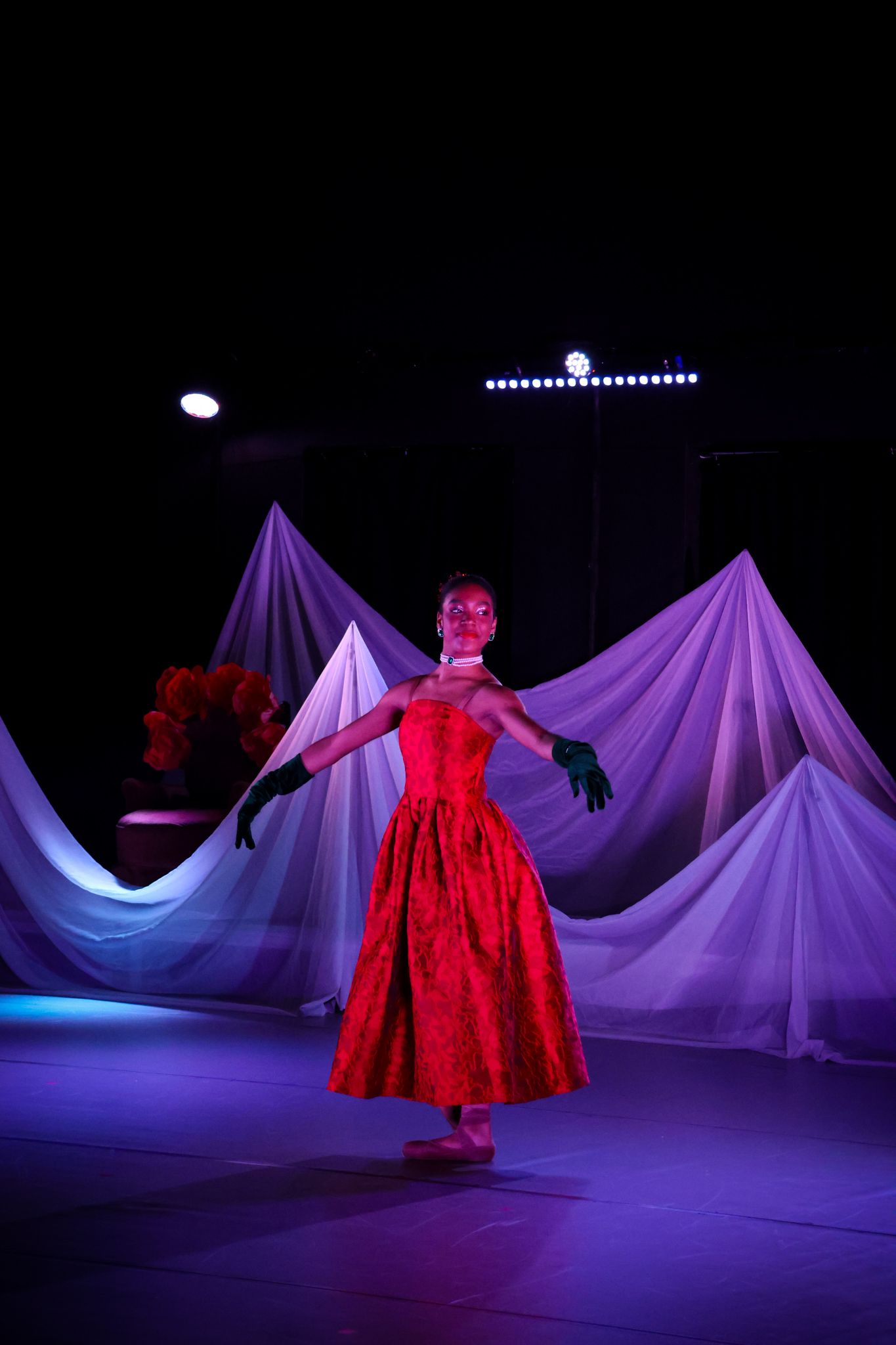 Theatrical performance featuring dancers in red dresses against purple draped fabric backdrops.