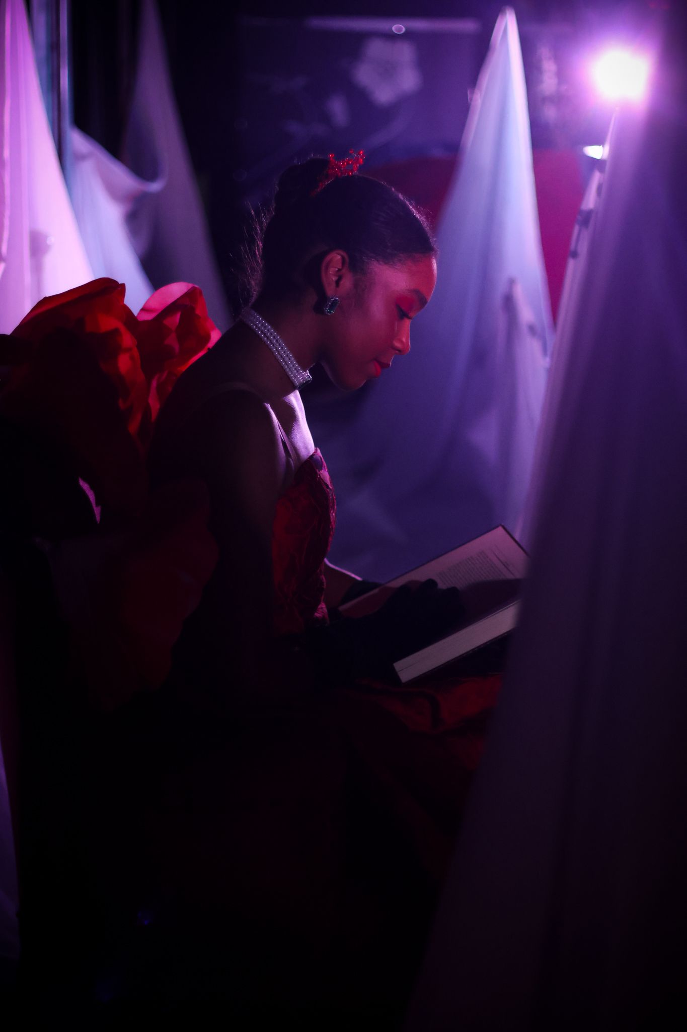 Dramatic stage performance with silhouetted figures reading in purple-tinted lighting.