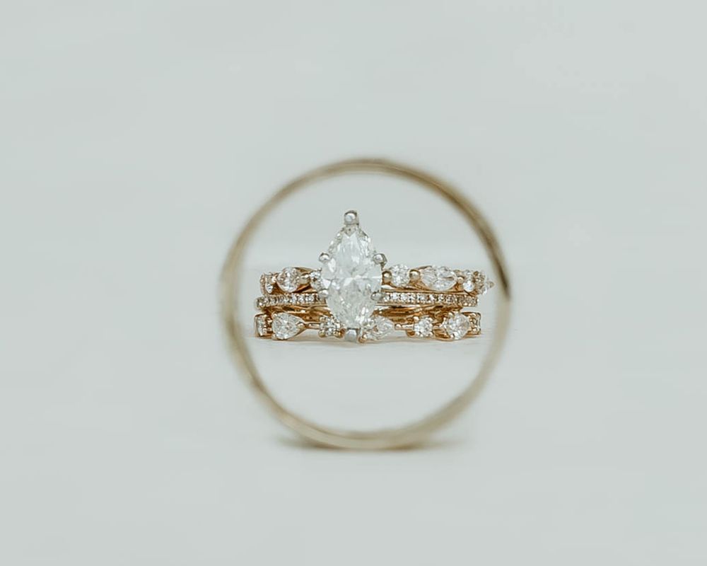 Delicate engagement ring and wedding bands sparkling against a white background in a panoramic display.