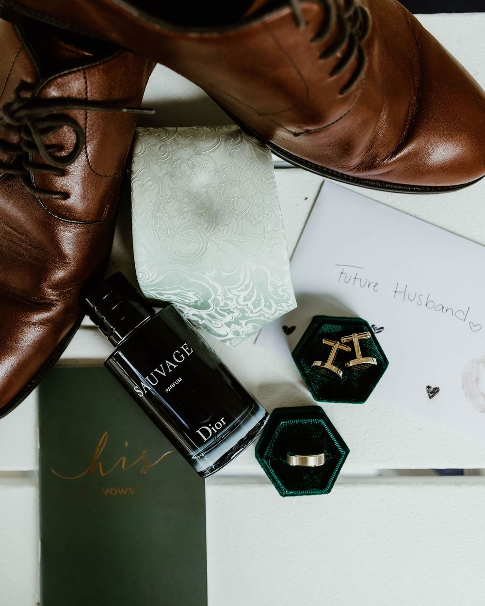 Brown leather shoes and black jewelry boxes arranged with elegant wedding stationery and decor.