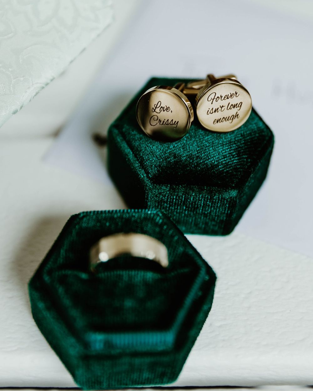 Wedding rings nestled in dark green velvet hexagonal ring boxes displaying elegant details.