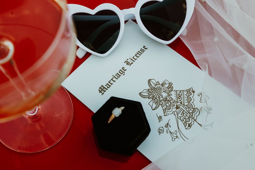Heart-shaped sunglasses with wedding details etched on white frame against red background.