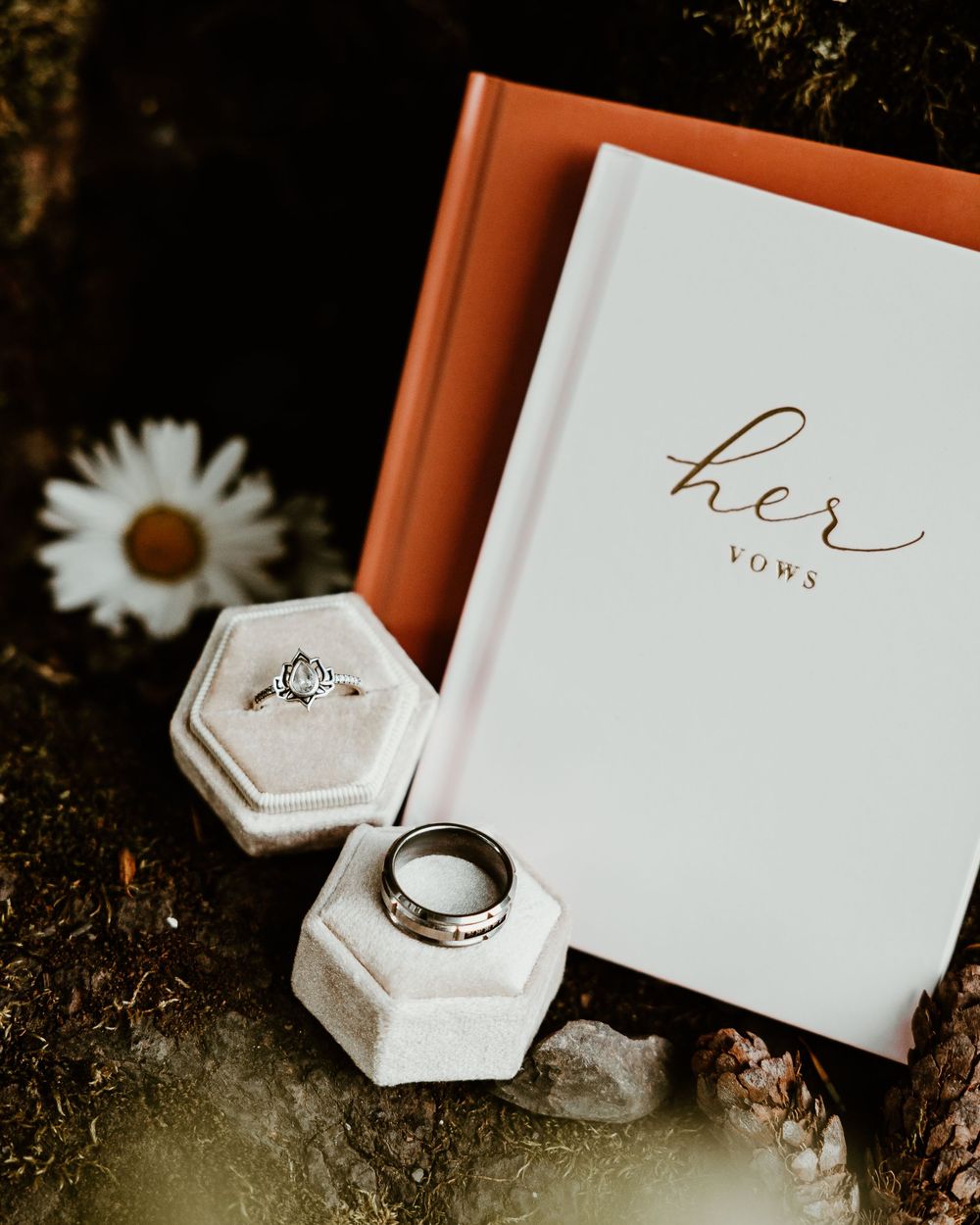 Wedding vow books and rings displayed with hexagonal ring box in artistic flatlay.