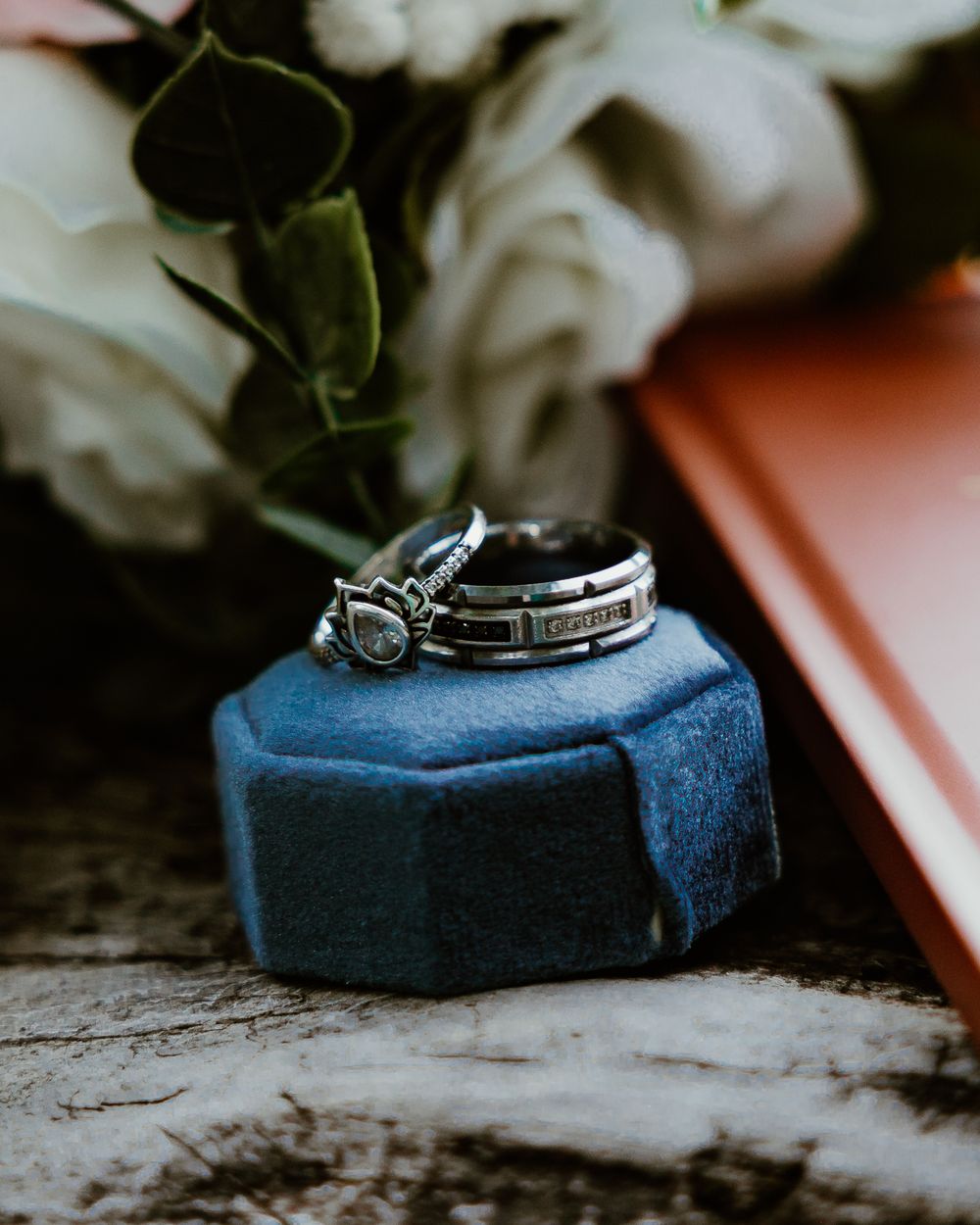 Wedding rings displayed on navy blue velvet ring box with white roses.